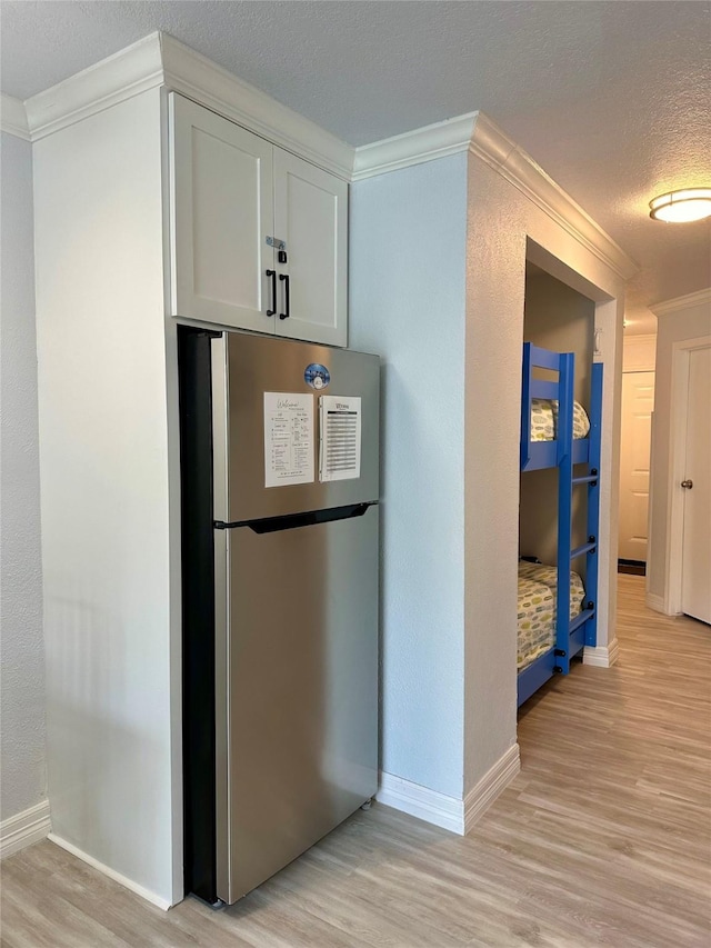 kitchen with ornamental molding, stainless steel fridge, a textured ceiling, white cabinets, and light hardwood / wood-style flooring