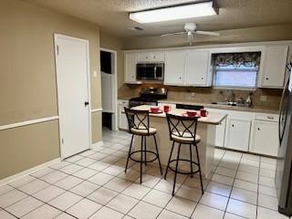 kitchen with stainless steel appliances, white cabinetry, a kitchen bar, and a kitchen island