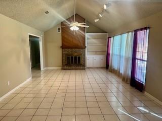 unfurnished living room with light tile patterned floors, a fireplace, ceiling fan, and vaulted ceiling