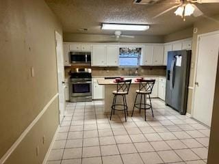 kitchen featuring stainless steel appliances, white cabinetry, a kitchen breakfast bar, light tile patterned floors, and a kitchen island