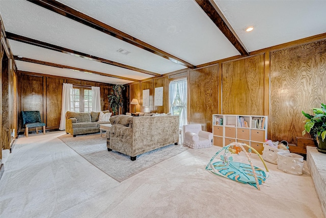 living room with wooden walls, a textured ceiling, beamed ceiling, and light colored carpet