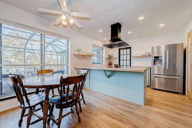 kitchen with a textured ceiling, light hardwood / wood-style floors, island exhaust hood, and stainless steel fridge