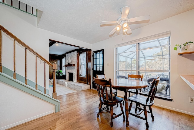 dining room featuring ceiling fan, light hardwood / wood-style flooring, a stone fireplace, and a textured ceiling