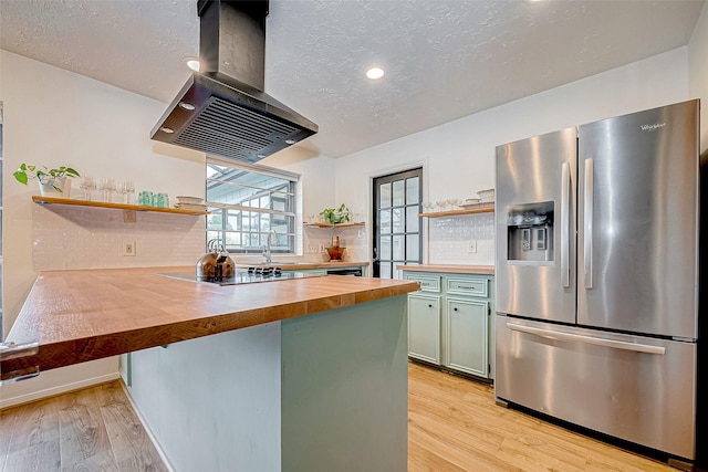 kitchen with island range hood, wood counters, kitchen peninsula, stainless steel fridge, and green cabinetry