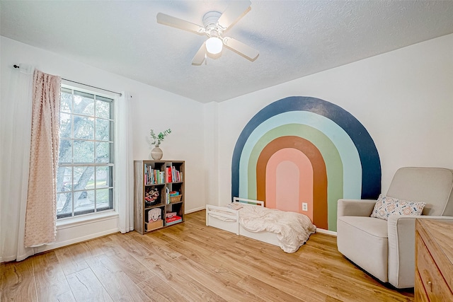 living area with a textured ceiling, ceiling fan, and light hardwood / wood-style flooring