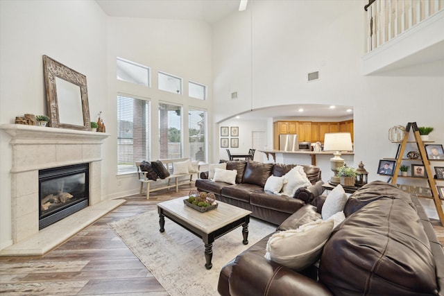 living room featuring a towering ceiling, a tiled fireplace, and light wood-type flooring