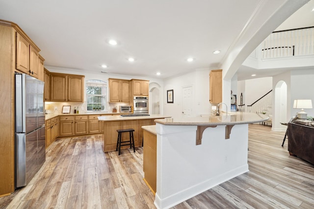 kitchen with stainless steel appliances, ornamental molding, a breakfast bar, and light hardwood / wood-style flooring