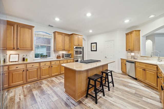 kitchen featuring sink, a center island, a kitchen breakfast bar, light hardwood / wood-style floors, and appliances with stainless steel finishes