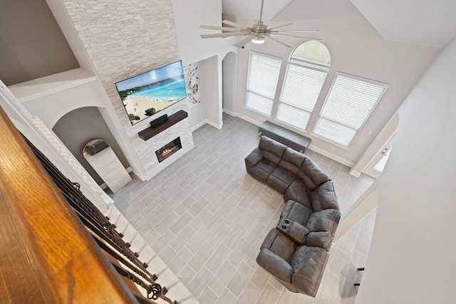 living room featuring a stone fireplace, a towering ceiling, tile patterned floors, and ceiling fan