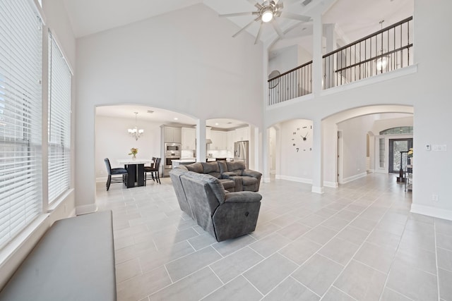 tiled living room with ceiling fan with notable chandelier and high vaulted ceiling