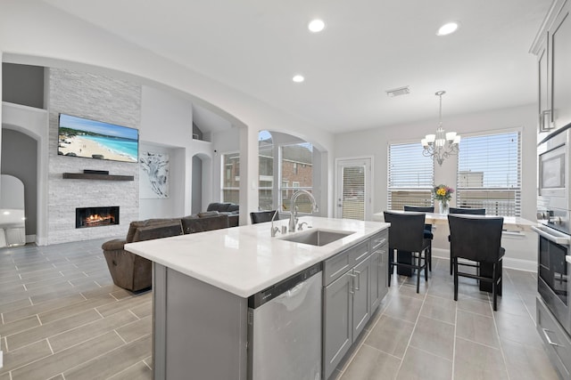 kitchen with a stone fireplace, sink, gray cabinetry, a center island with sink, and stainless steel appliances