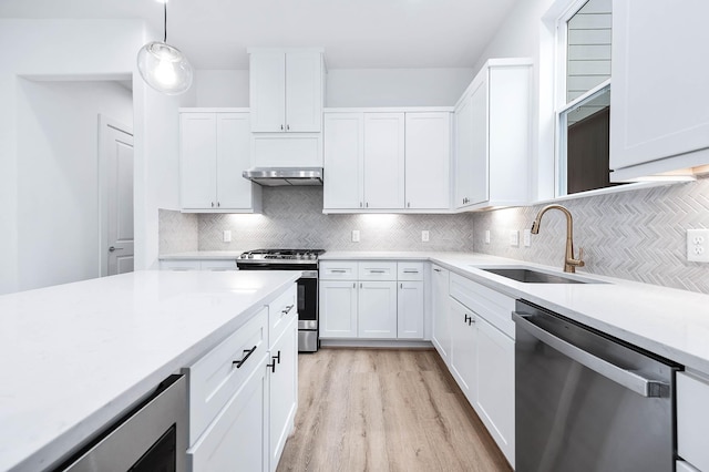 kitchen featuring stainless steel appliances, decorative backsplash, sink, white cabinetry, and decorative light fixtures