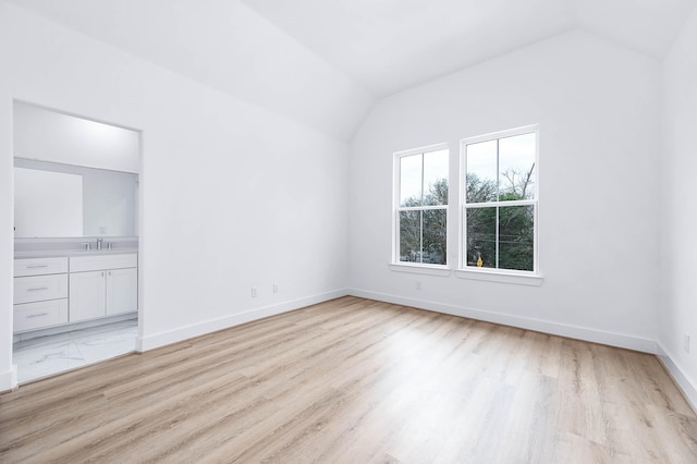 interior space with lofted ceiling, ensuite bath, sink, and light hardwood / wood-style floors