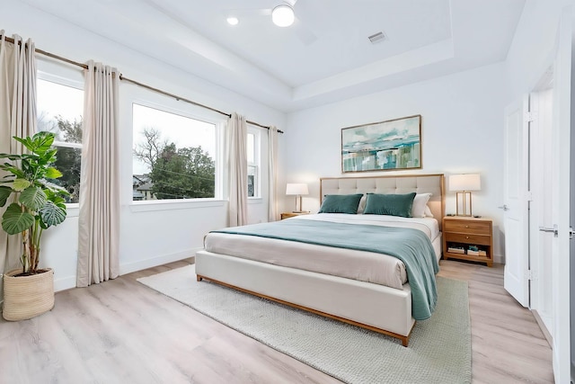 bedroom with a raised ceiling, multiple windows, light wood-type flooring, and ceiling fan