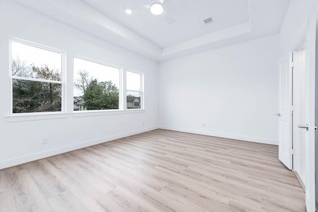 unfurnished room featuring ceiling fan, light wood-type flooring, and a tray ceiling