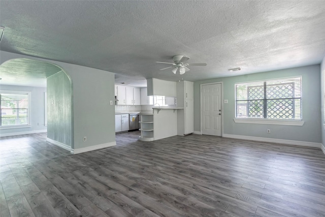 unfurnished living room featuring ceiling fan, a wealth of natural light, and dark hardwood / wood-style floors