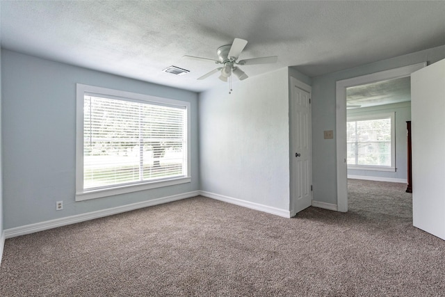 carpeted spare room with a textured ceiling, ceiling fan, and a healthy amount of sunlight