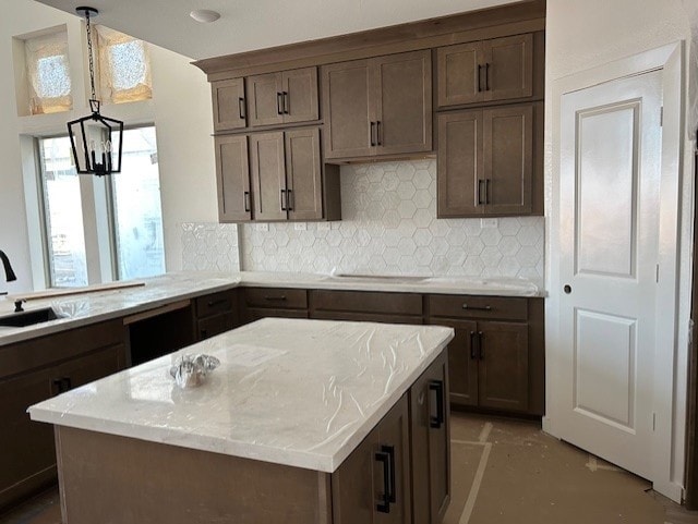 kitchen featuring kitchen peninsula, pendant lighting, light stone counters, sink, and tasteful backsplash