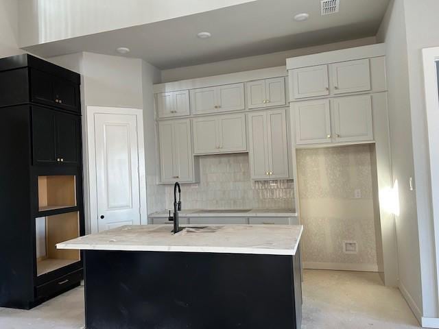 kitchen with white cabinetry, a kitchen island with sink, and tasteful backsplash