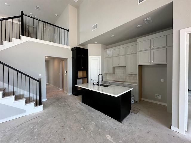 kitchen featuring a sink, cooktop, tasteful backsplash, visible vents, and an island with sink