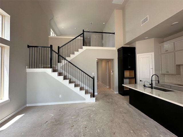 kitchen featuring a sink, tasteful backsplash, visible vents, baseboards, and a towering ceiling