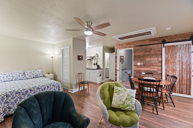 bedroom featuring ensuite bath, ceiling fan, hardwood / wood-style floors, a barn door, and wood walls