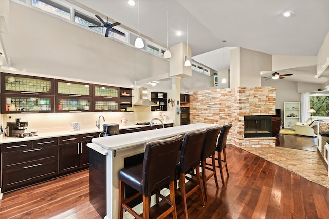 kitchen with dark hardwood / wood-style floors, high vaulted ceiling, a fireplace, a breakfast bar area, and wall chimney range hood