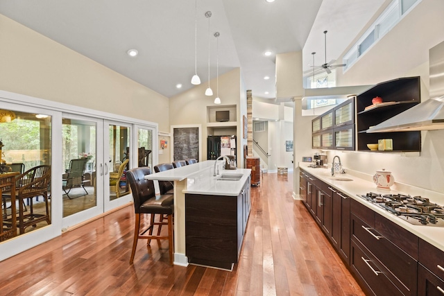 kitchen with sink, hanging light fixtures, high vaulted ceiling, stainless steel gas cooktop, and a center island with sink