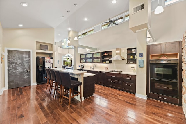 kitchen with wall chimney exhaust hood, a breakfast bar, black appliances, a center island, and a high ceiling