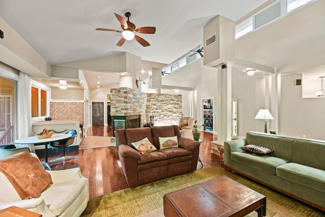 living area featuring high vaulted ceiling, hardwood / wood-style floors, a stone fireplace, ceiling fan, and ornate columns