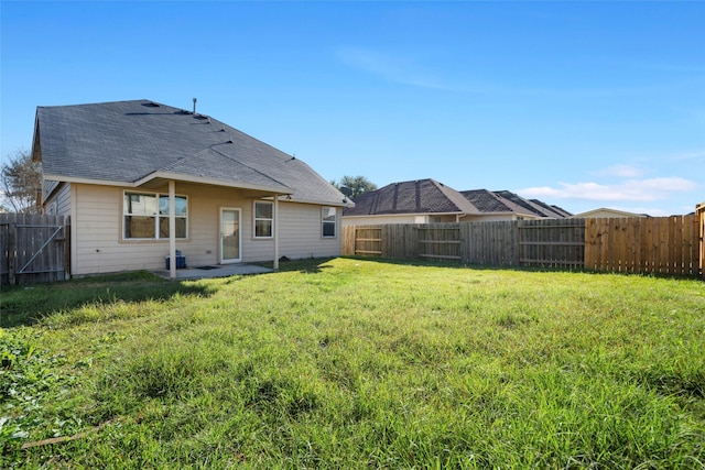 back of property featuring a fenced backyard, a yard, and a shingled roof