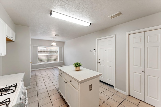 kitchen with pendant lighting, a center island, light tile patterned floors, white gas stove, and white cabinets