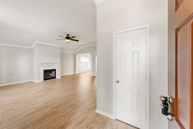 unfurnished living room with ceiling fan, ornamental molding, vaulted ceiling, and a tiled fireplace