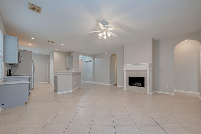 unfurnished living room with a tiled fireplace, ceiling fan, light tile patterned flooring, and sink