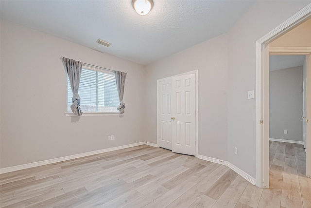 unfurnished bedroom with a closet, a textured ceiling, and light hardwood / wood-style flooring