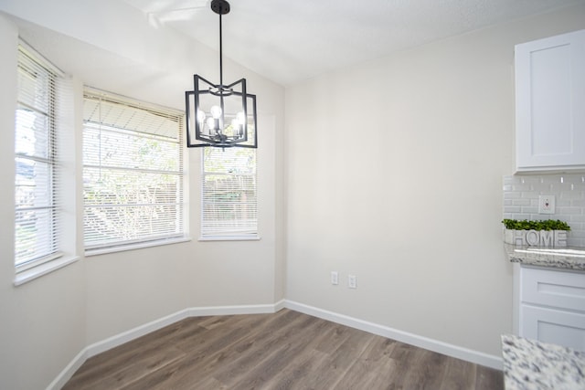 unfurnished dining area featuring lofted ceiling, a notable chandelier, and dark hardwood / wood-style floors