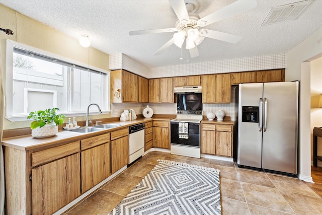 kitchen featuring white appliances, a sink, visible vents, light countertops, and brown cabinetry