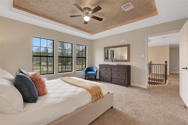 carpeted bedroom with ceiling fan, a tray ceiling, and crown molding