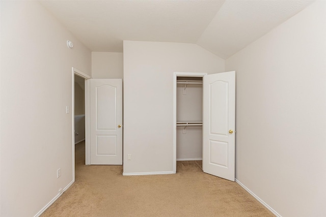 unfurnished bedroom featuring light colored carpet, vaulted ceiling, and a closet