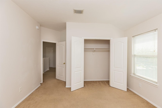 unfurnished bedroom featuring light colored carpet, lofted ceiling, and a closet