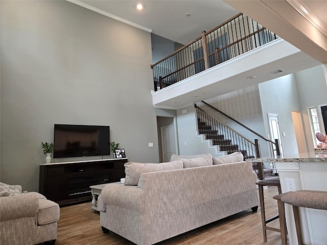 living room with ornamental molding, light hardwood / wood-style flooring, and a towering ceiling