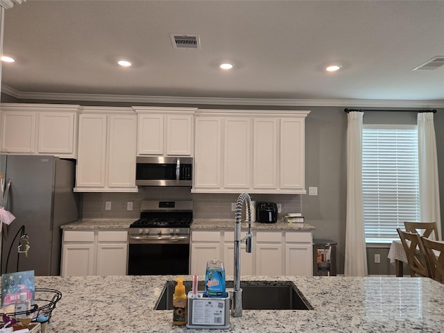 kitchen featuring sink, white cabinets, light stone counters, ornamental molding, and appliances with stainless steel finishes