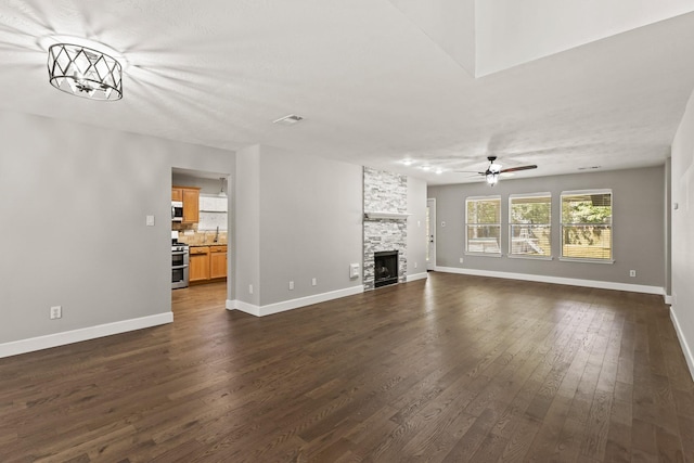 unfurnished living room with ceiling fan, dark hardwood / wood-style flooring, a stone fireplace, and sink