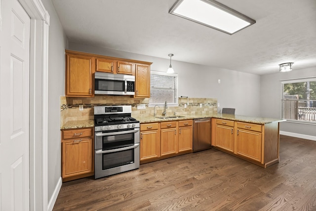 kitchen featuring kitchen peninsula, pendant lighting, dark hardwood / wood-style floors, stainless steel appliances, and sink