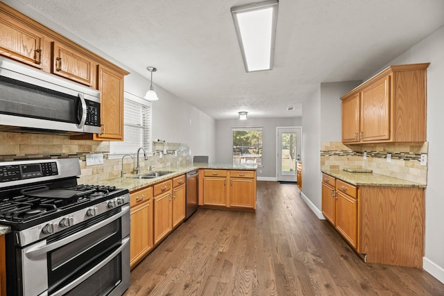 kitchen featuring stainless steel appliances, hanging light fixtures, kitchen peninsula, dark wood-type flooring, and sink