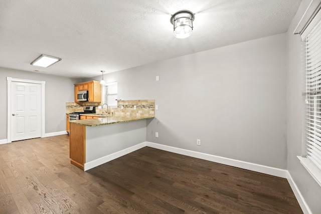 kitchen featuring hardwood / wood-style floors, appliances with stainless steel finishes, hanging light fixtures, kitchen peninsula, and backsplash