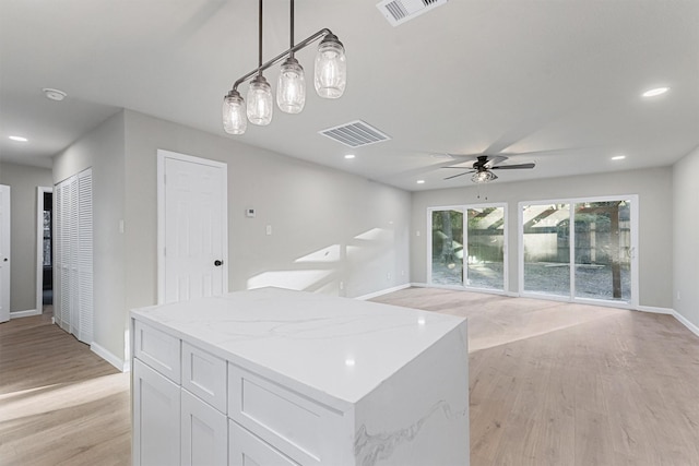 kitchen featuring decorative light fixtures, light wood-type flooring, white cabinets, and light stone countertops