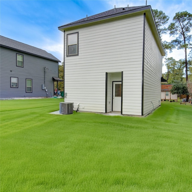 rear view of property featuring a lawn and cooling unit