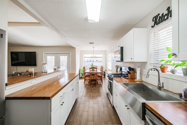 kitchen with sink, a textured ceiling, white cabinetry, wooden counters, and appliances with stainless steel finishes