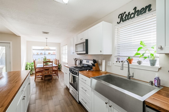 kitchen with hanging light fixtures, stainless steel appliances, butcher block counters, white cabinetry, and sink